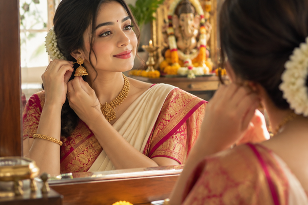 Indian woman wearing traditional gold jhumka earrings and saree while getting ready for festive occasion