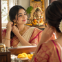 Indian woman wearing traditional gold jhumka earrings and saree while getting ready for festive occasion