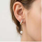 Close-up side view of a model wearing the gold plated wave pearl drop earring, showcasing the delicate crystal pave arc and linear drop pearl design.