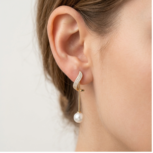 Close-up side view of a model wearing the gold plated wave pearl drop earring, showcasing the delicate crystal pave arc and linear drop pearl design.