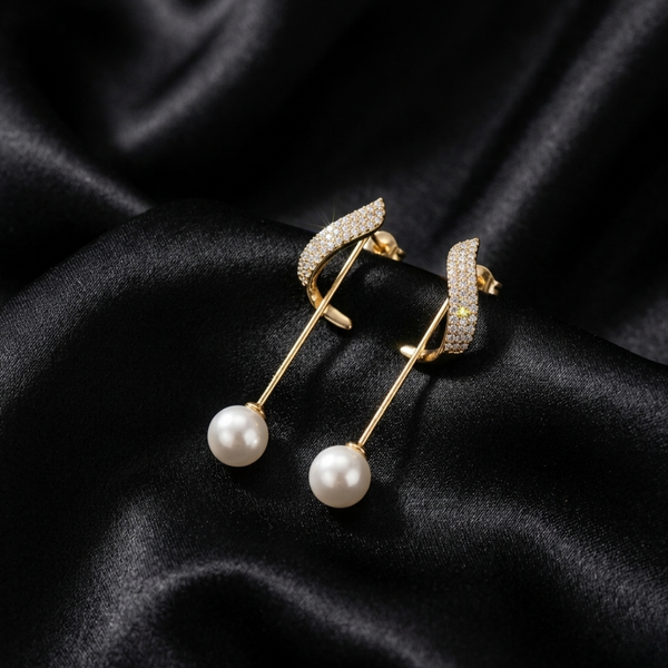 Close-up detail of gold-plated wave pearl drop earrings with brilliant pave crystals displayed on black silk.