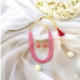 Blush Pink beaded necklace and earrings styled on cream fabric.