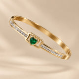 Close-up studio shot of the Jwanas Emerald-Green Heart Bangle Bracelet on a beige background