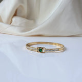 Jwanas Emerald-Green Heart Bangle Bracelet placed on a white surface with cream fabric behind