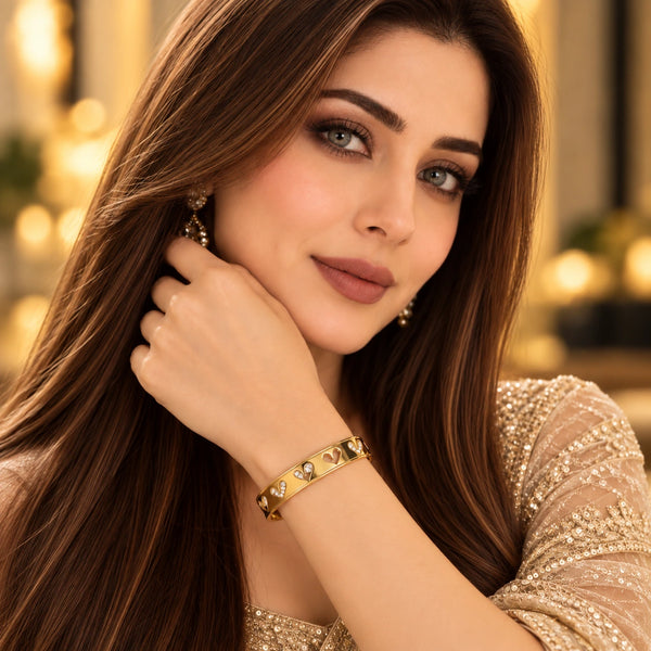 Model wearing Jwanas Gold Heart Charm Bangle Bracelet paired with an elegant beige embellished outfit.