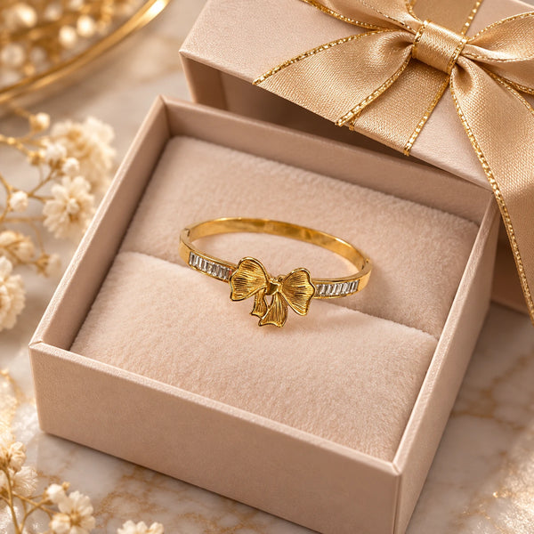 Jwanas Golden Bow Baguette Bangle Bracelet displayed inside an open gift box with a gold ribbon bow