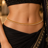 Model wearing the Jwanas Golden Pearl Elegance Waist Chain with white pearl drops styled with a black saree and gold embroidery.