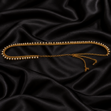 Jwanas Golden Pearl Elegance Waist Chain arranged on black satin, showcasing its gold-tone chain and delicate white pearl detailing.