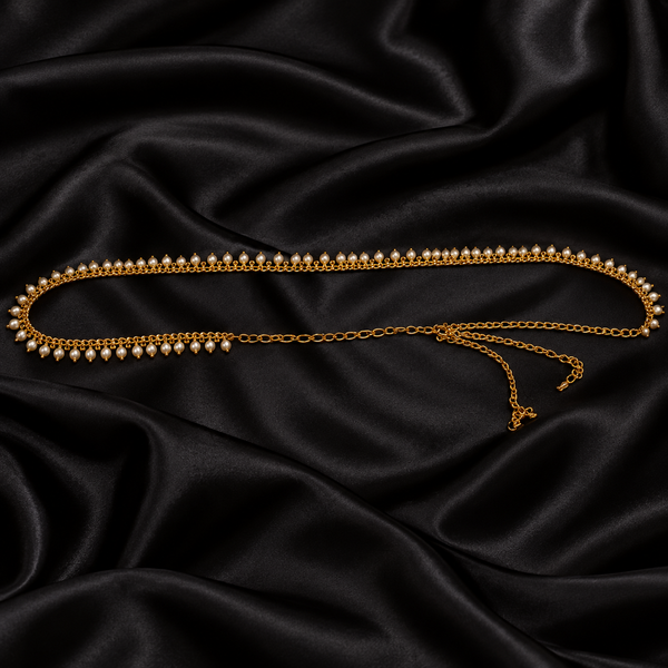 Jwanas Golden Pearl Elegance Waist Chain arranged on black satin, showcasing its gold-tone chain and delicate white pearl detailing.