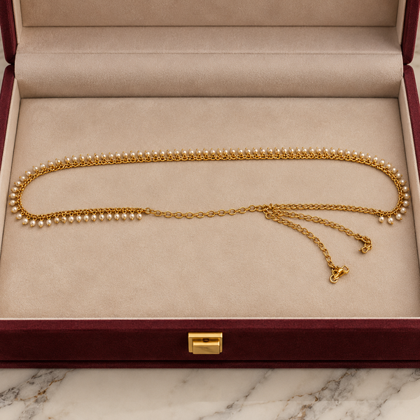 Jwanas Golden Pearl Elegance Waist Chain displayed in a cream-lined burgundy velvet jewellery box, featuring white pearl drops and an adjustable gold-tone chain.