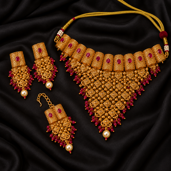 Jwanas Rani Ruby-Toned Bridal Choker Set with earrings and Maang Tikka displayed as a flat lay on black satin