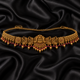 Jwanas Royal Lakshmi Temple Gold Kamarbandh featuring intricate temple motifs, ruby-red accents, and dangling gold beads displayed on black satin.